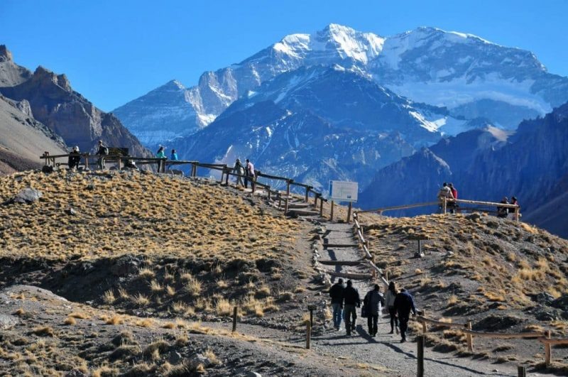 Pessoas andam em direção a um mirante no parque. Nota-se montanhas cobertas de neve ao fundo.